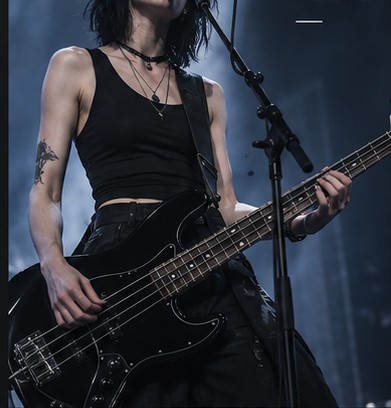 Vanta performing on bass under stage lighting, a tattoo visible on her forearm.
