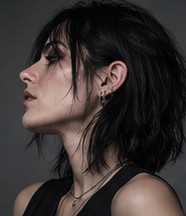 Profile portrait of Vanta, dark hair falling across her face, small silver earrings visible.